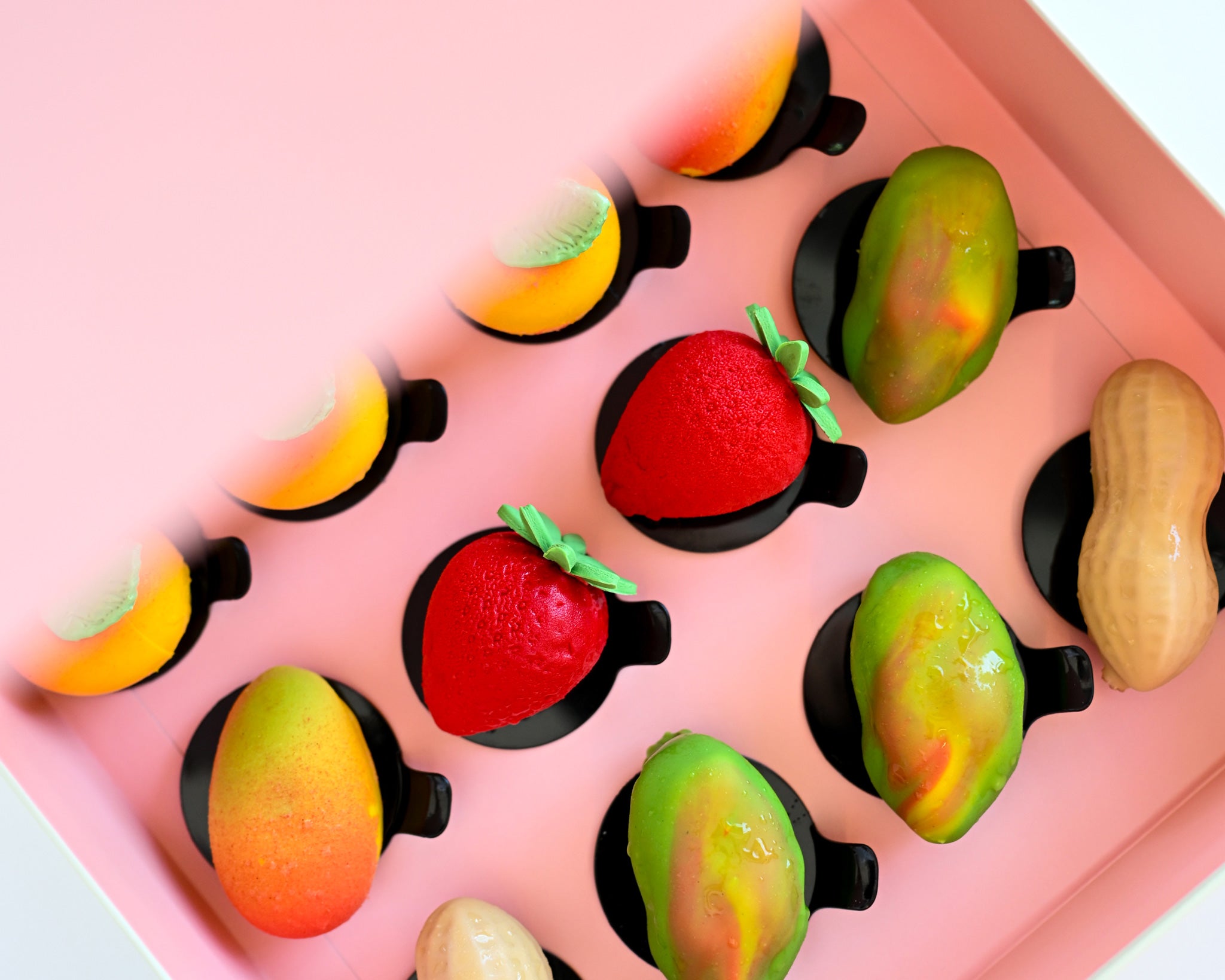 A pink gift box filled with vibrant fruit-shaped mini pastries.