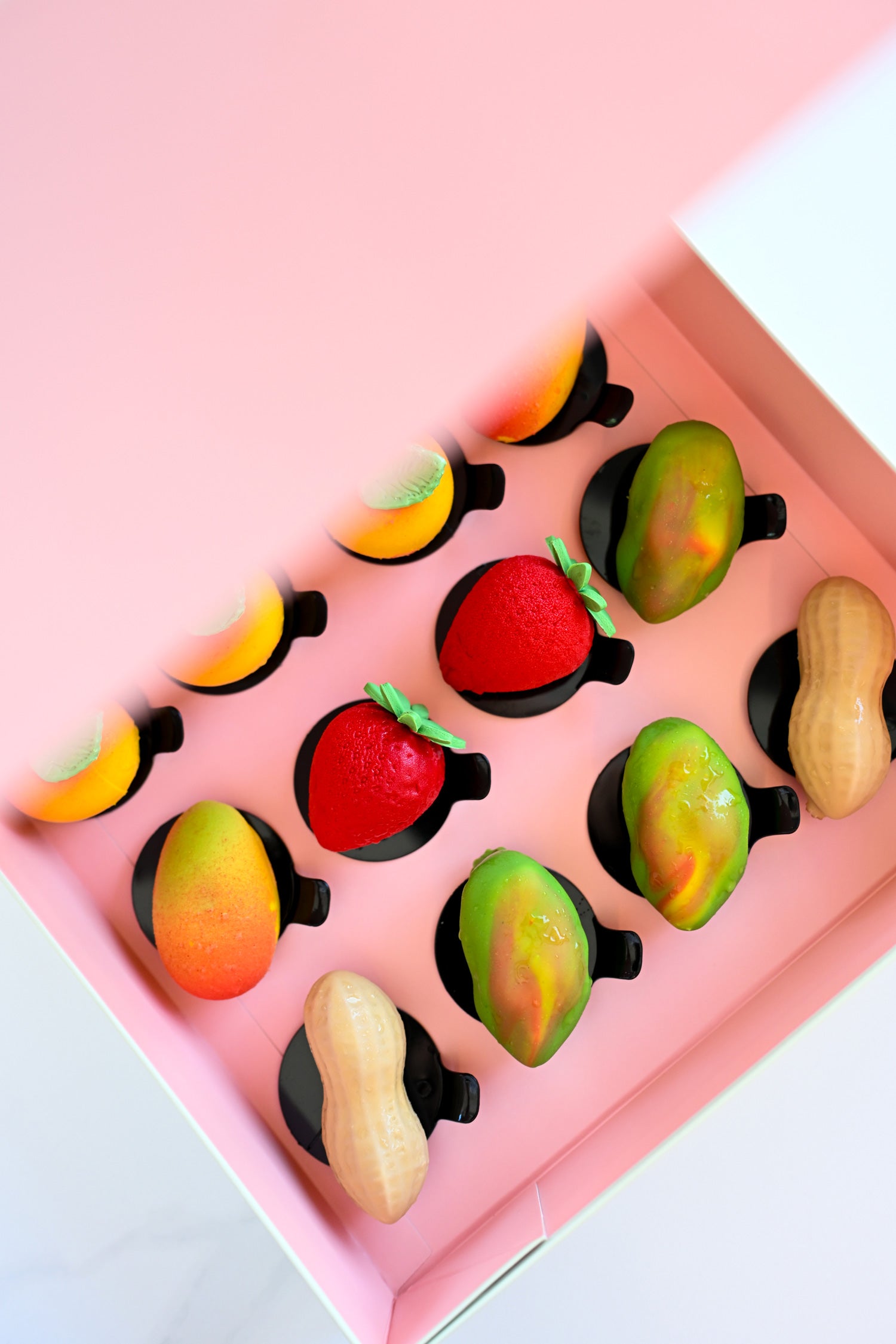 A pink gift box filled with vibrant fruit-shaped mini pastries.